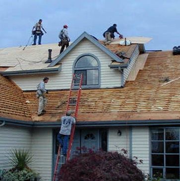 Workers replace a house roof with new wooden shingles.