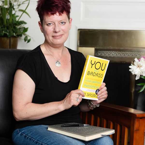 Woman sitting on a chair holding a book titled 'You Are a Badass'.