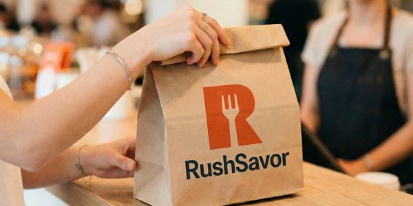 A person handing over a RushSavor branded paper bag at a counter.