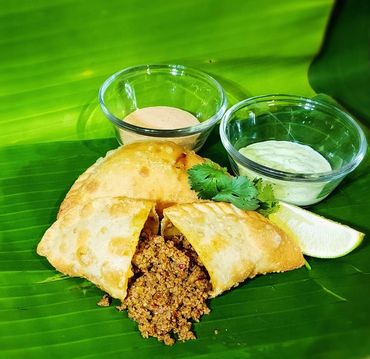 Crispy stuffed pastry with sauces on a banana leaf.