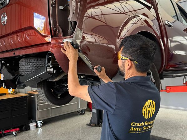 Technician repairing a red pickup truck in an auto service shop.