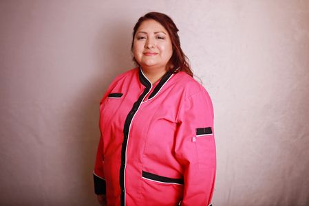 A woman wearing a pink chef jacket smiles gently at the camera.