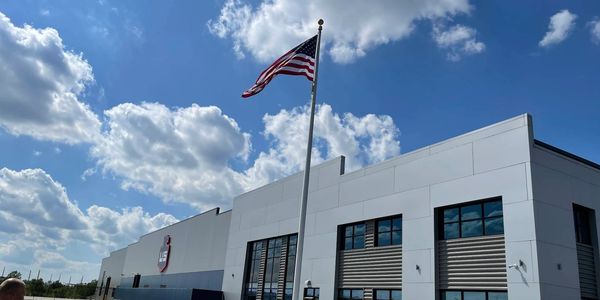 the exterior of a large gray warehouse with the American flag raised upon a pole