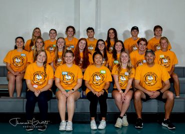 Group of young people wearing matching orange shirts posing indoors.