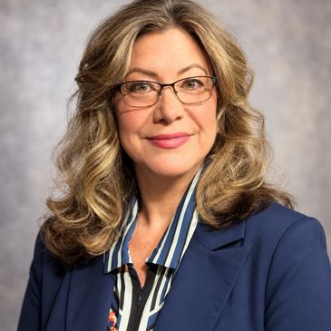 Professional woman with glasses and curly hair wearing a blazer.