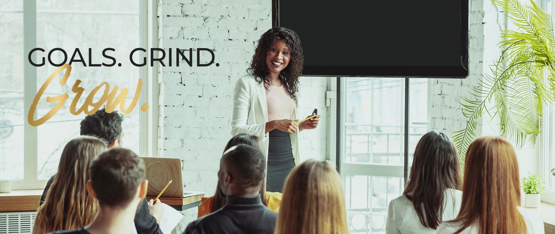 Woman presenting to a diverse group with motivational words on the wall.