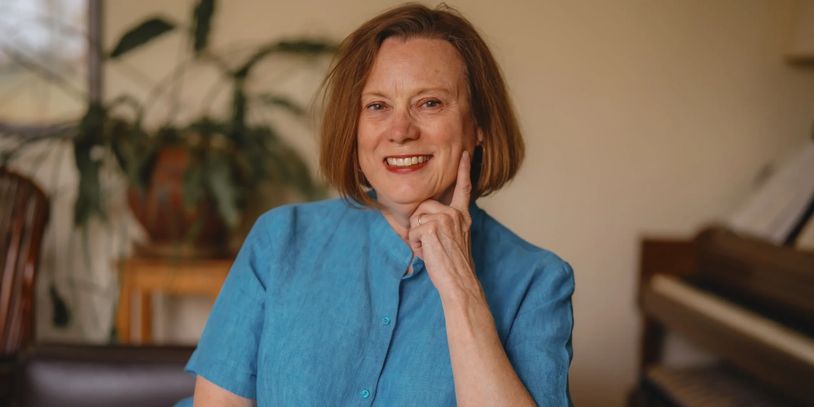 Smiling woman in blue shirt posing indoors with a thoughtful gesture.
