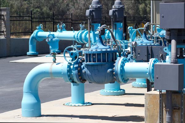 Exterior view of a water pump station with various blue pipes, valves, and gray motor housings.