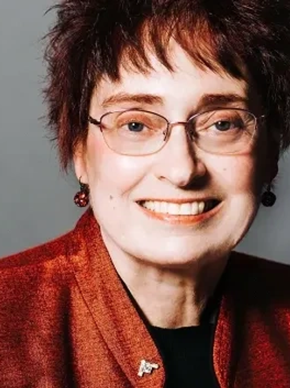 Smiling older woman with glasses and red attire.