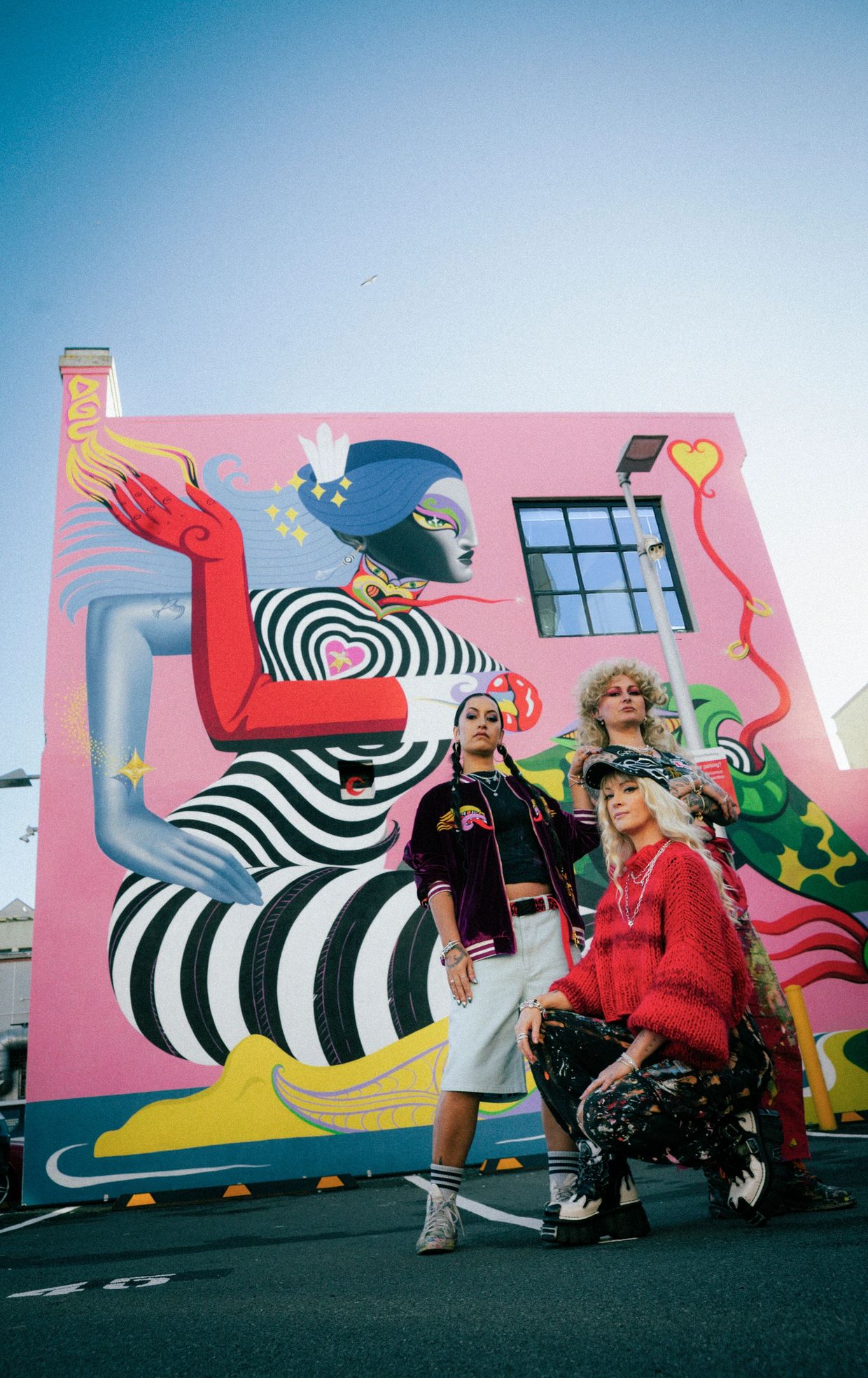 Three stylish women pose in front of a vibrant street mural.