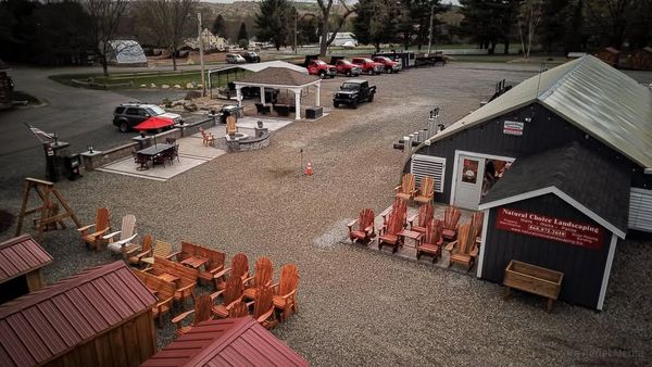 Outdoor furniture display with wooden chairs and a pavilion in a gravel lot.