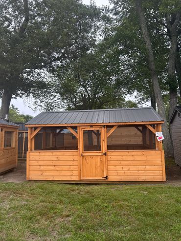 Wooden screened-in porch or gazebo with a metal roof in a grassy area.