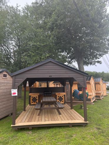 Wooden outdoor pavilion with picnic table and grill under a dark roof.
