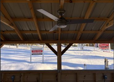 View from a wooden shelter showing snow-covered ground and advertising signs.