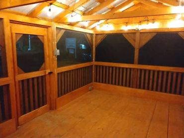 Cozy wooden porch with string lights and screened windows at night.