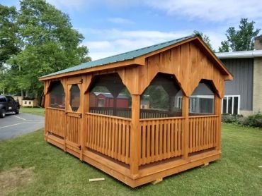 Wooden screened gazebo with green metal roof on grass.