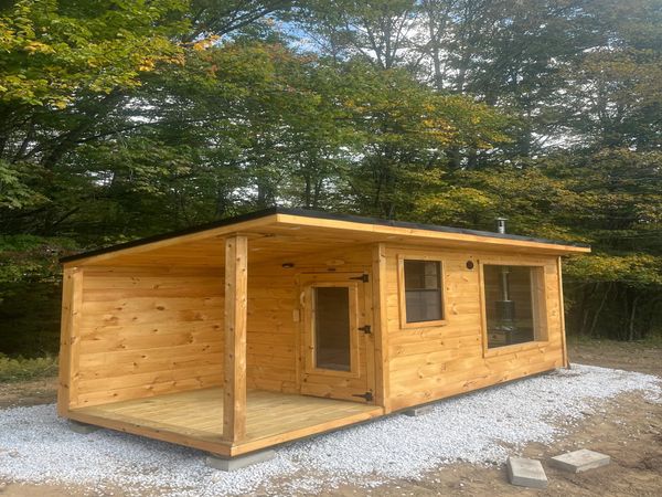 A small wooden cabin with a porch surrounded by trees.
