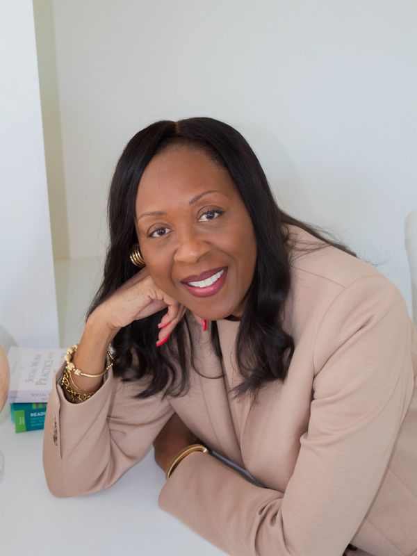Smiling woman in beige blazer resting her head on her hand.