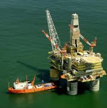 Offshore oil rig with a supply vessel beside it in calm waters.