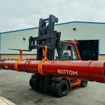 Forklift carrying a large red pipe labeled 'BOTTOM' outside a warehouse.