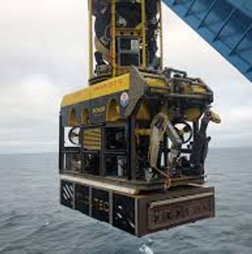 A yellow underwater remotely operated vehicle being lowered into the ocean.