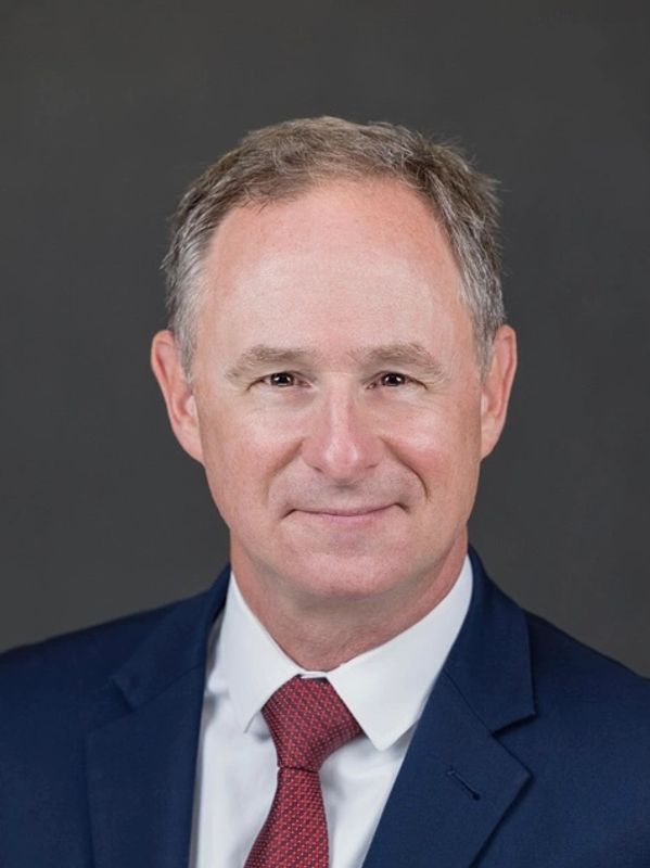 Professional headshot of a middle-aged man in a blue suit and red tie.