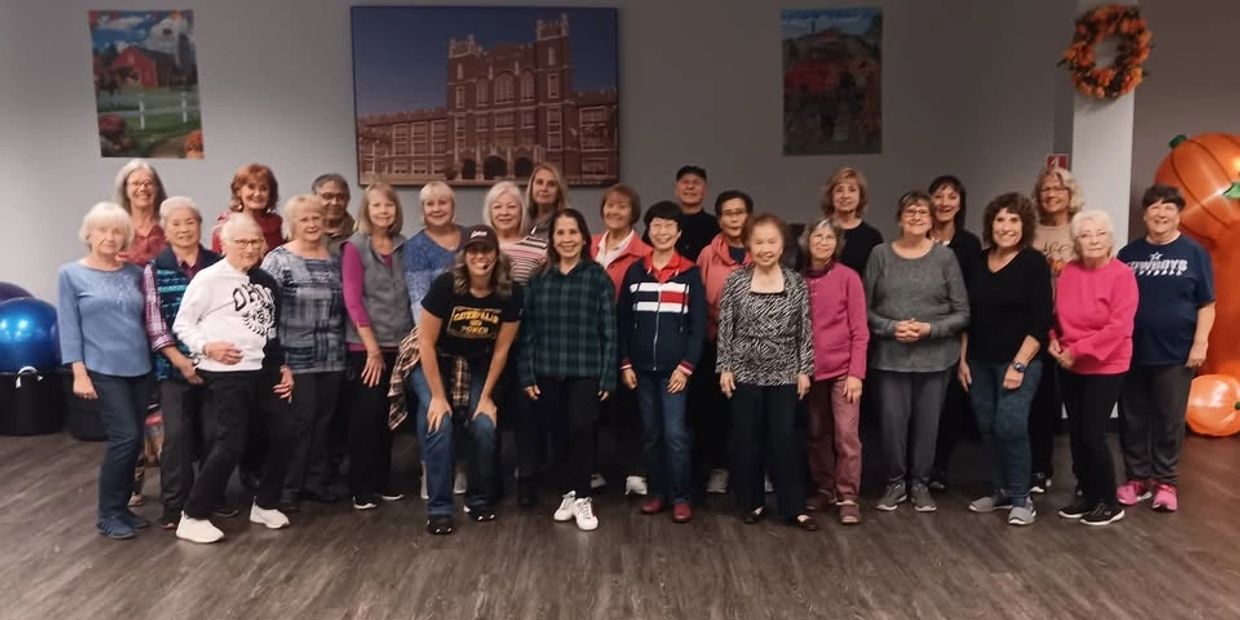 A group of diverse older adults posing together indoors on a wooden floor.
