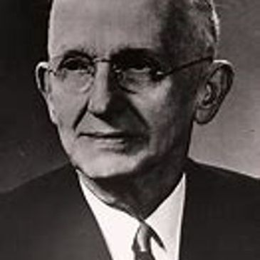 Black and white portrait of an elderly man wearing glasses and a suit.