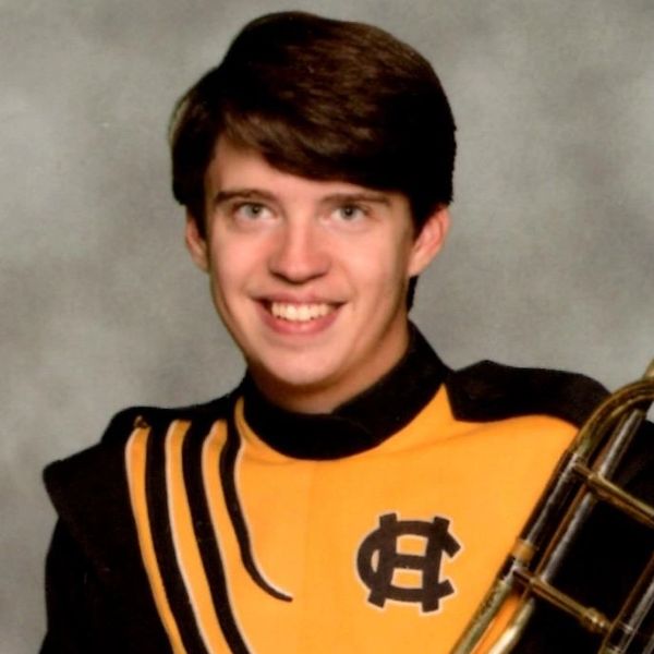 Young man in a yellow and black band uniform smiling.