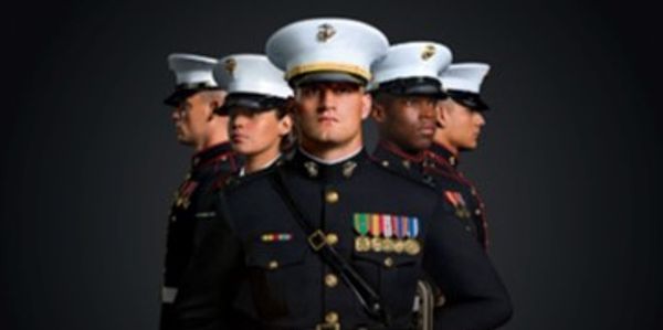 Five Marines in dress blues standing in a V formation with serious expressions.