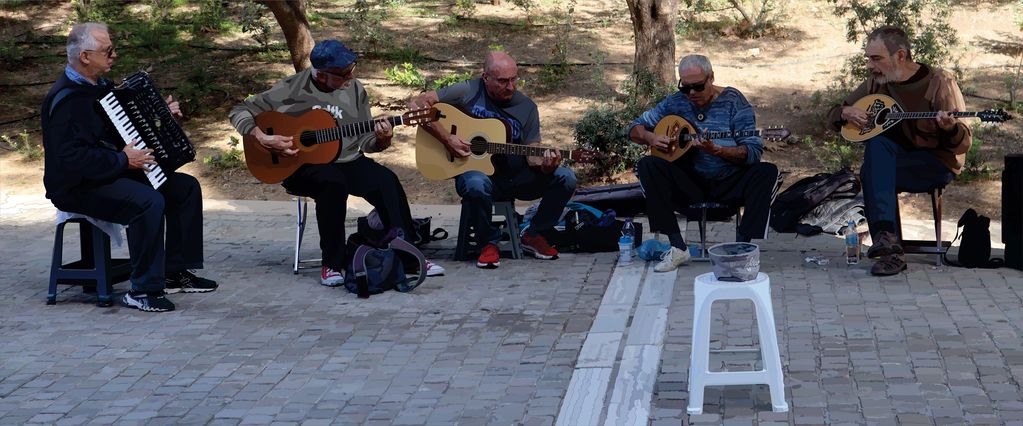 Five men playing musical instruments outdoors in a park.