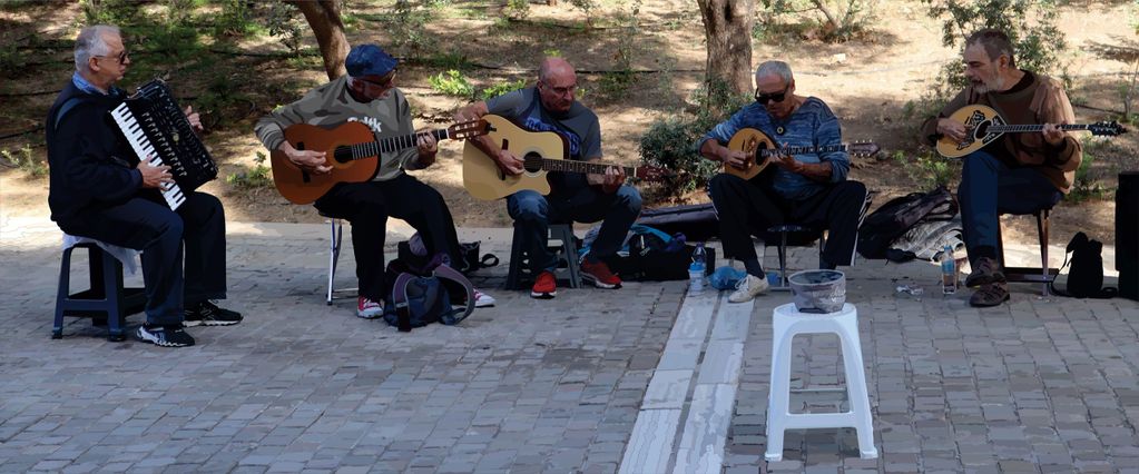 Five men playing musical instruments outdoors in a park.