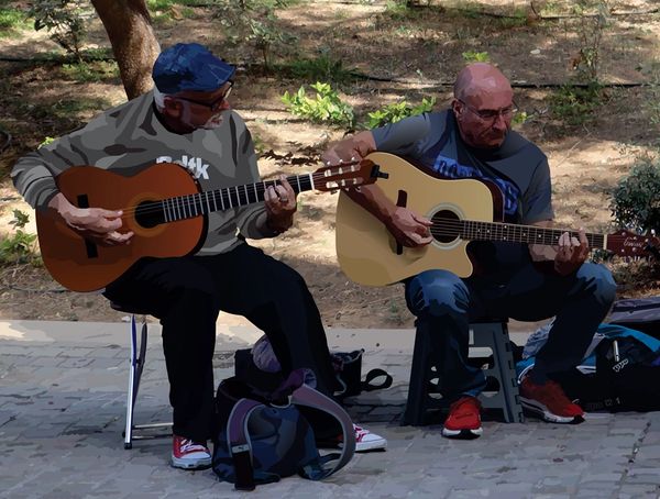 Two men playing acoustic guitars while sitting outdoors.