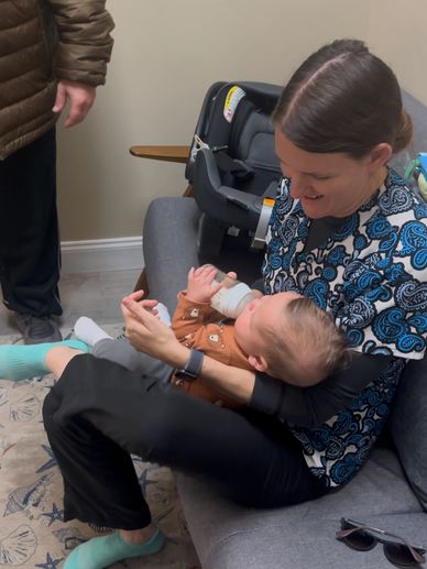 A woman feeding a baby with a bottle while sitting on a couch.