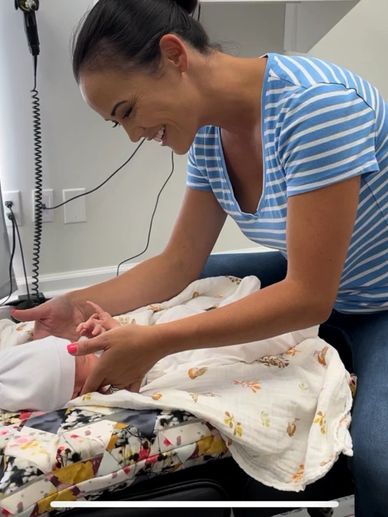 A woman joyfully interacts with a newborn baby wrapped in a blanket.