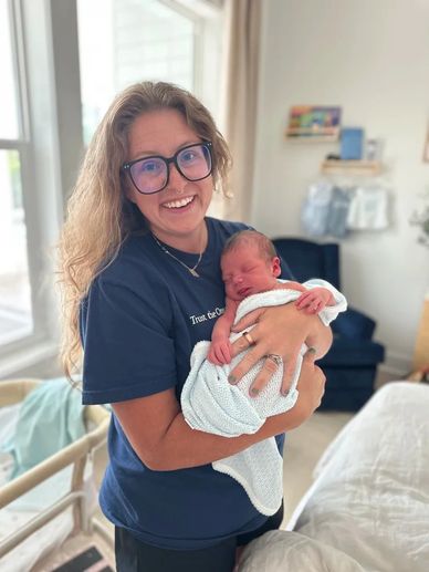 Smiling woman holding a newborn wrapped in a blanket indoors.