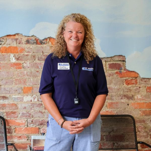 Smiling volunteer in a navy blue shirt standing against a brick wall.