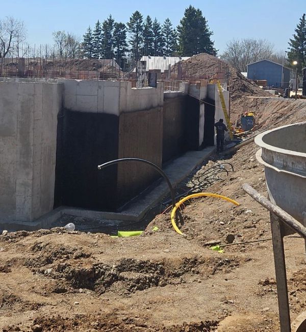 Construction site with concrete walls and workers applying waterproofing.