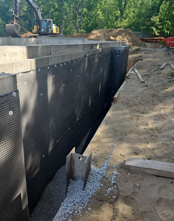 Construction site showing foundation waterproofing and gravel drainage installation.