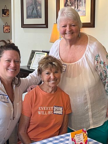 Three smiling women gathered indoors, wearing name tags and casual clothes.