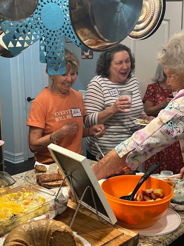 Women enjoying food and conversation in a cozy kitchen gathering.