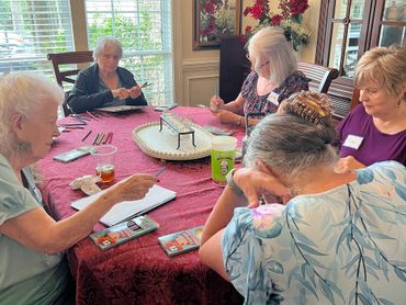 A group of elderly women engaged in a crafting activity around a table.