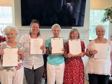 Five women proudly holding their portrait drawings in a cozy living room.