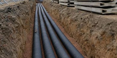Large black pipes laid in a trench at a construction site.