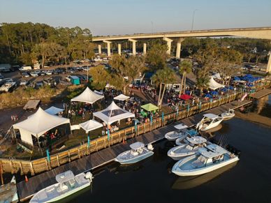 Outdoor event with tents and boats docked near a waterfront under a clear sky.