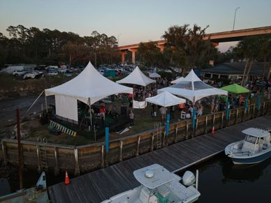 Outdoor event with white tents near a waterfront and boats at dusk.