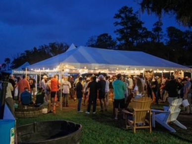 Crowd gathered under a lit tent at dusk for an outdoor event.