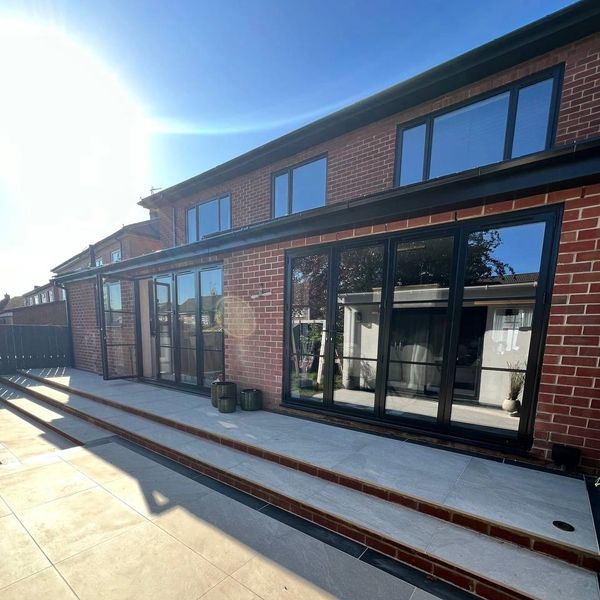 Modern brick house with large glass doors and clean tiled patio under bright sunlight.