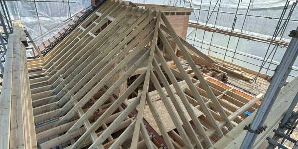 Wooden framework of a roof under construction inside a scaffolded area.
