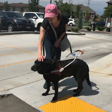 Photo of woman with black guide dog on yellow truncated dome.